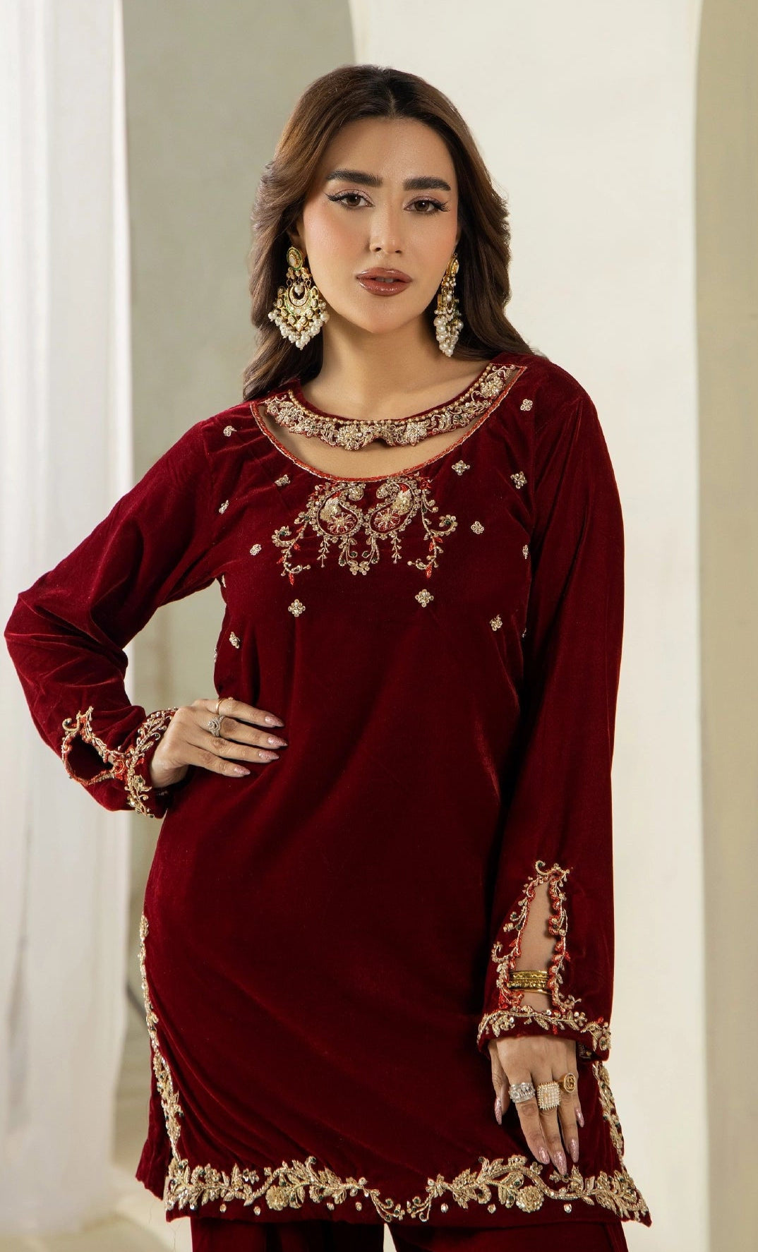 A woman modeling a deep maroon velvet kurta with intricate gold and silver embroidery around the neckline, sleeves, and hem, paired with matching Maroon Farshi trousers.